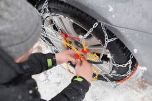 man putting chains on his tires in the snow
