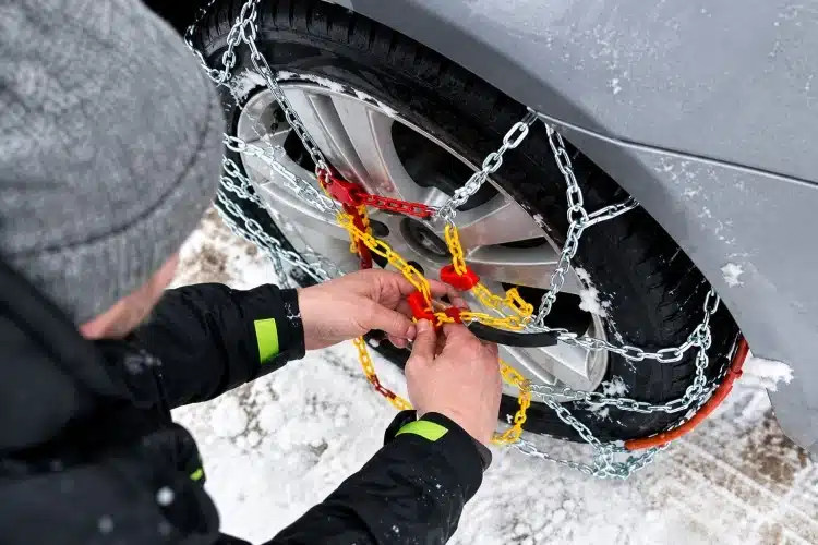 man putting chains on his tires in the snow